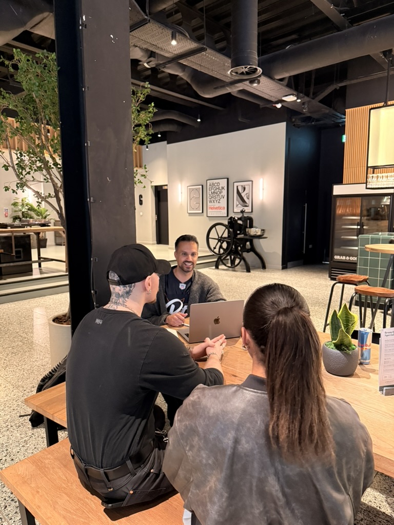Three colleagues discussing AI work around a laptop in a modern office
